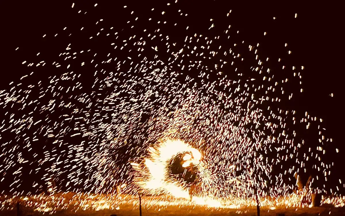 A performer spinning a wide arc of fire sparks in the dark