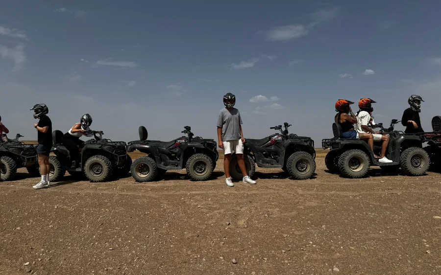 Riders standing beside a row of quad bikes on stony desert ground