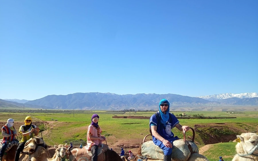 Riders on camels in green fields with the Atlas range behind