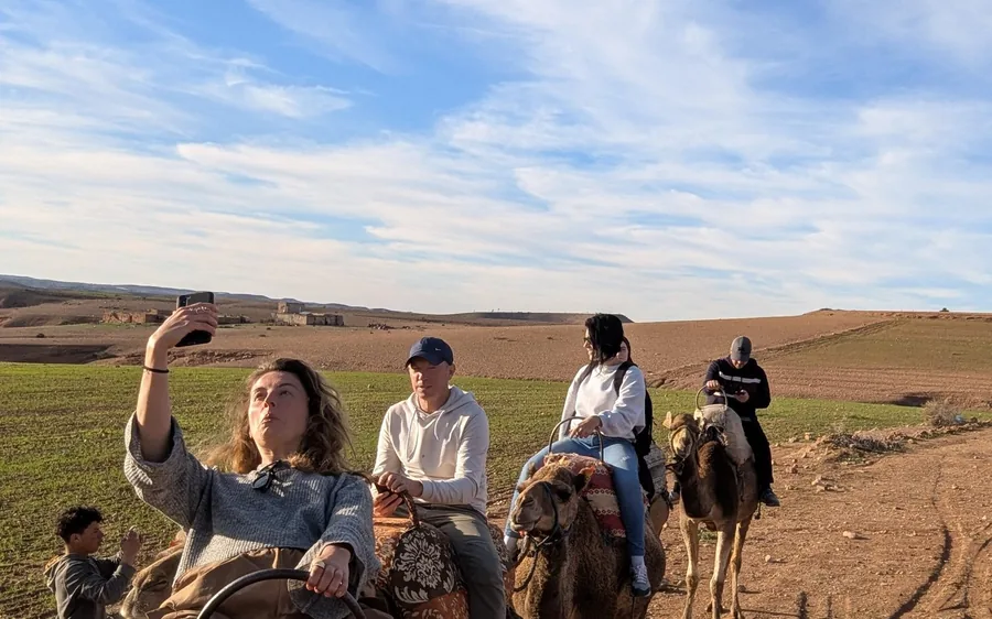 Visitors on camels taking photos in green countryside