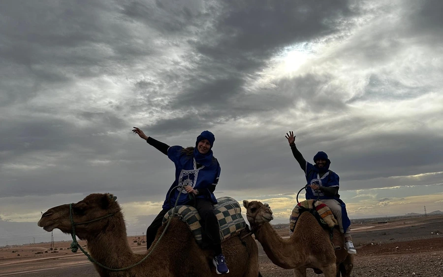 Two riders in blue robes raising their arms on camels under cloud