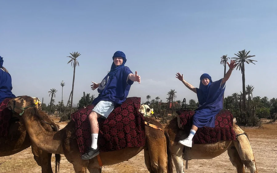 Riders in blue robes waving from camels among palm trees