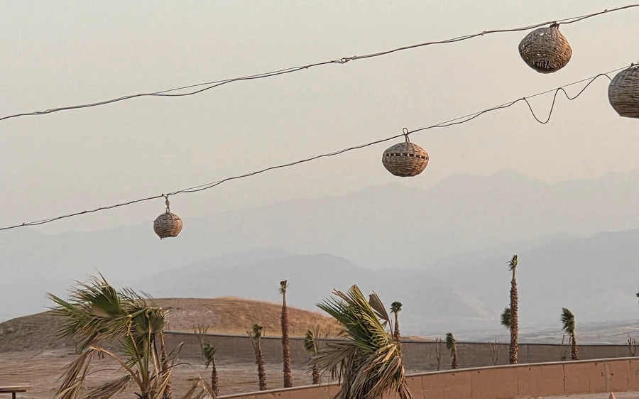 Lanterns strung over a desert camp with hazy hills behind