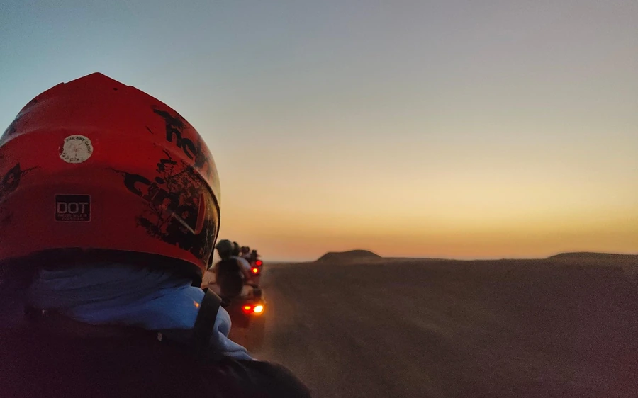 A rider in a red helmet on a quad facing the setting sun