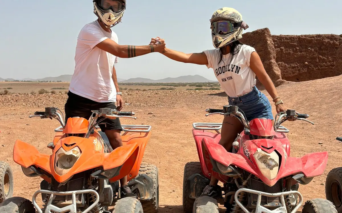 Two riders in goggles on quad bikes bumping fists on stony ground